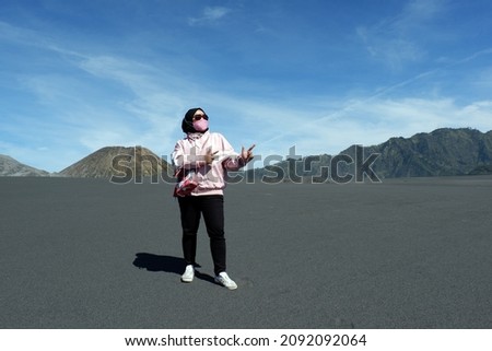 Hijab woman wearing sunglasses pointing up both hands below the unique cloud shape.