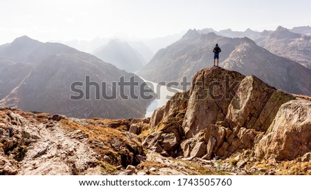 Hiker or alpinist at the top of a mountain. A success of mountaineer reaching the summit. Outdoor adventure sports alpine moutain landscape. Sunny day and a adventure man on a top of a peak.