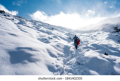 
				Hiker ascent to the summit. Winter ice and snow climbing in mountains. A success of mountaineer reaching the summit. Outdoor adventure sports in winter alpine moutain landscape.