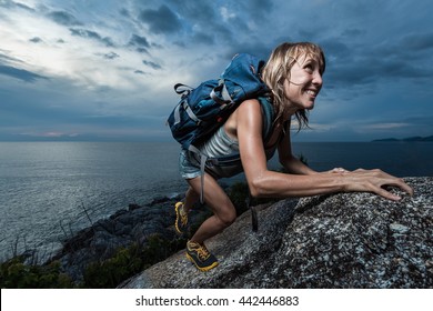 Hiker with backpack climbing natural rocky wall on a dark cloudy background. There are water drops on the skin