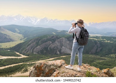 Hiker with backpack looking in binoculars on top of mountains at sunset. - Powered by Shutterstock