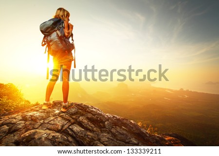 Hiker with backpack relaxing on top of a mountain and enjoying valley view during sunrise