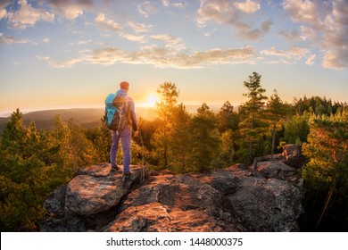 Hiker with backpack standing on a rock and enjoying sunset on mauntain