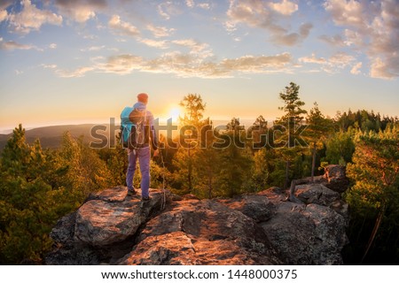 Hiker with backpack standing on a rock and enjoying sunset on mauntain