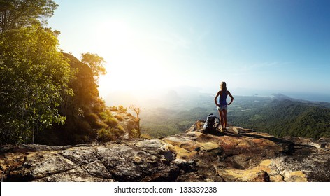Hiker with backpack standing on top of a mountain and enjoying stunning valley view