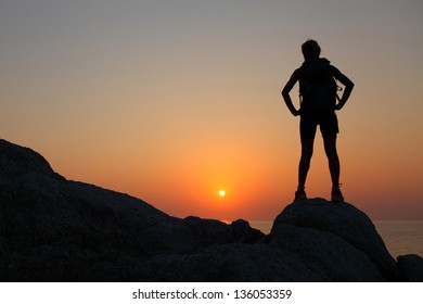 Hiker With Backpack Standing On Top Of A Mountain And Enjoying Sunset