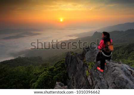 Hiker with backpack standing on top of the mountain and enjoying valley view at sunrise.Asia woman standing  and watching towards the sea of fog at sunrise. Asia woman look for next destination