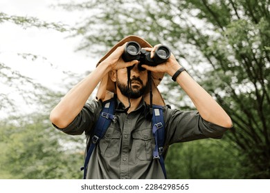 Hiker with backpack using binoculars in the wild. Field biologist or naturalist using binoculars to study wildlife or nature.
