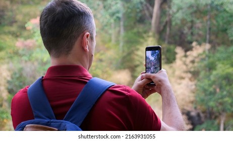 Hiker blogger or vlogger man in woods shooting forest. Male traveler videographer with backpack, standing in nature and filming video on smartphone camera