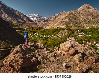 Hiker blonde girl standing over green mountain valley of Imlil in High Atlas Mountains during spring season, Morocco, Africa