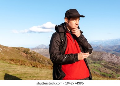 Hiker with a cap using an application to guide himself in the mountains. person holding a smartphone. mountain sports and activities. weekend getaway and free time.