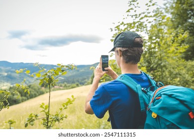 Hiker capturing the beauty of nature on a smartphone at sunset, standing in a grassy meadow with a forest backdrop. A blend of adventure, technology, and tranquility. - Powered by Shutterstock