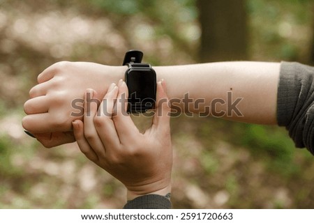 Hiker checking her smartwatch while enjoying a peaceful walk through the lush woods, blending modern technology with the tranquility of nature and enhancing her outdoor experience