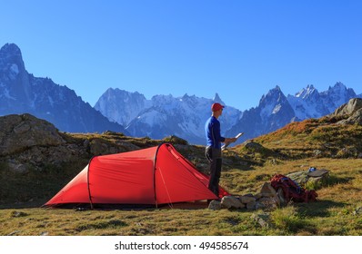 Hiker Checking A Map At His Red Tent In The Mountains Near Chamonix, France.