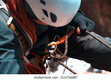 A hiker, a climber in a white helmet descends on a rope down the cliff, a close-up view of a hand in a fleece glove, with which a man holds on to a rock ledge. - Shutterstock ID 2115756887