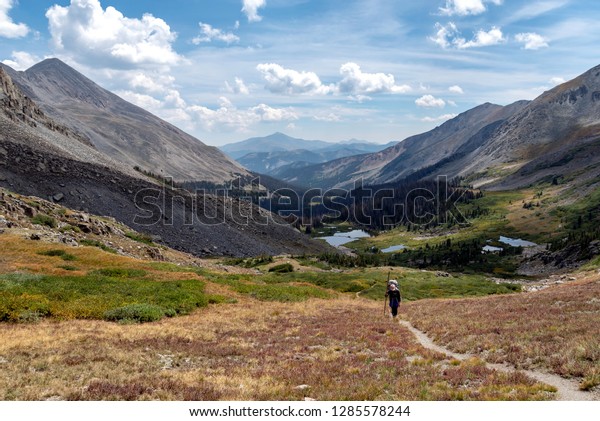 A hiker climbs the last few\
steps to the summit of a pass overlooking a beautiful valley in the\
rocky mountains. A remote and peaceful place in the wilderness.\
