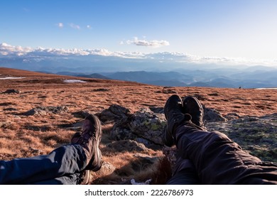 Hiker couple legs resting on alpine meadow with panoramic view on mountains seen from Ladinger Spitz, Saualpe, Lavanttal Alps, Carinthia, Austria, Europe. Trekking in the Austrian Alps on a sunny day