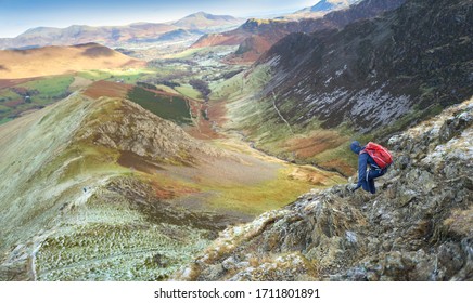 A Hiker Descending The Steep Rocky Mountain Ridge From The Summit Of Robinson Towards High Snab Bank On A Cold Winters Day With Scope Beck Below In The Lake District, UK.