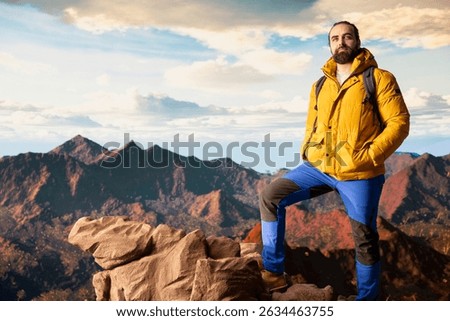Hiker gazes at the panoramic view of dramatic mountain peaks and clouds, feeling the thrill of adventure and rewards of perseverance. The journey represents strength and personal growth.