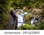 hiker girl crossing the bridge over a rushing river with waterfalls on the way to famous lake marian in fiordlands national park, new zealand south island