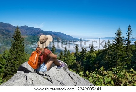 Hiker girl sitting on a cliff edge enjoying scenic summer view. Woman relaxing on top of the mountain, over the clouds. Blue Ridge Parkway ,near Asheville, North Carolina, USA.
