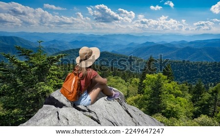 Hiker girl sitting on a cliff edge enjoying scenic summer view. Woman relaxing on top of autumn mountain, over the clouds. Blue Ridge Parkway ,near Asheville, North Carolina, USA.
