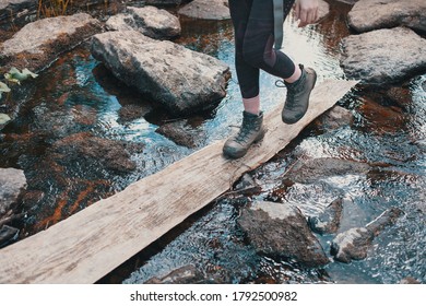 Hiker girl wades across the river on a wooden Board, heavy Hiking boots