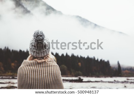 Hiker girl wrapping in warm blanket outdoor. Hiking in mountains in autumn. Bad weather with fog. Cold morning by the river.