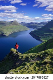 Hiker In A Hike On Eysturoy Island Overlooking The Funningur Fjord On Faroe Islands, Denmark. Summer Sunny Day