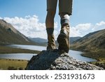 Hiker legs wearing leather boots hiking on high altitude mountain top,with a lake in the distance