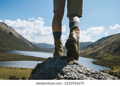 Hiker legs wearing leather boots hiking on high altitude mountain top,with a lake in the distance - Powered by Shutterstock