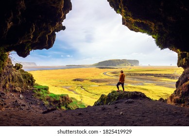 Hiker in the Loftsalahellir Cave near the village of Vik overlooking the beautiful landscape of Iceland with a road passing by.