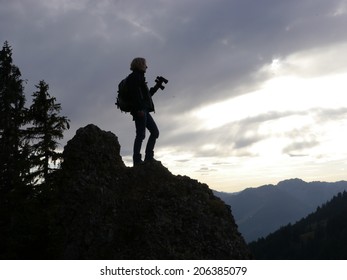 Hiker looking in binoculars enjoying spectacular view on mountain top above the clouds.