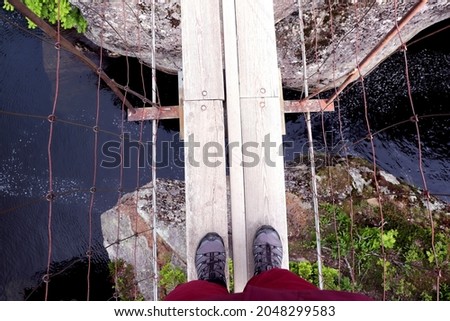Hiker looking down at feet at river below on a rope bridge in Norway