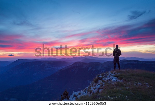 ハイカーが山の多い荒野で静かでピンクの夕日を見ている の写真素材 今すぐ編集