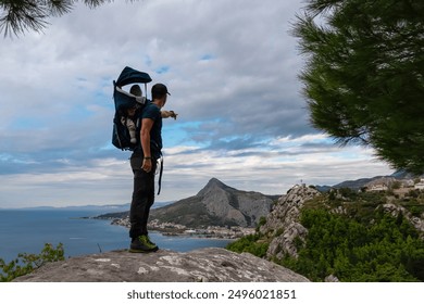 Hiker man with baby carrier backpack on rock formation with aerial view of coastal town Omis, Dinara mountains, Split-Dalmatia, Croatia, Europe. Coastline of Adriatic Sea, Balkans. Travel destination - Powered by Shutterstock