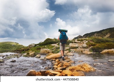 Hiker man with backpack crossing a river on stones in bulgarian mountains. Hiking and leisure theme. Image with sunlight effect
