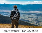 Hiker man climbed on the mountain top. Guy stands on the mountain hilltop. Scenic view to Kootenay valley, Creston, British Columbia, Canada