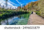 Hiker man sitting on enchanting hiking trail on rustical wooden footpath in Plitvice lakes National Park, Karlovac, Croatia, Europe. Bridge over turquoise water in idyllic paradise nature. Wanderlust