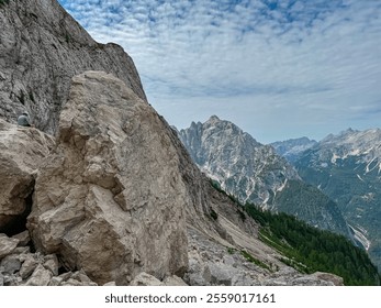 Hiker man sitting on massive rock formation with panoramic view of rugged mountain ridge Prisank in majestic Julian Alps. Adventure and freedom in Triglav National Park, Slovenia, Slovenian Alps - Powered by Shutterstock