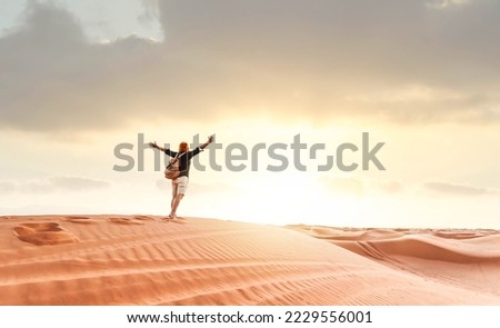 Hiker man walking in the desert sand dunes at sunset - Happy traveler with arms up enjoying freedom outside - Wanderlust, wellbeing, happiness and travel concept