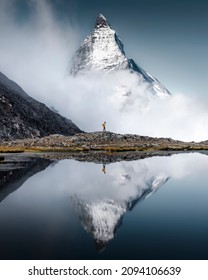Hiker man walks alone through the incredible Swiss Alps with the Matterhorn in the background between clouds and mystery while it is reflected in the Riffelsee lake - Shutterstock ID 2094106639