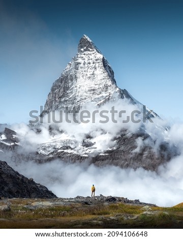 Hiker man walks alone through the incredible Swiss Alps with the Matterhorn in the background between clouds and mystery