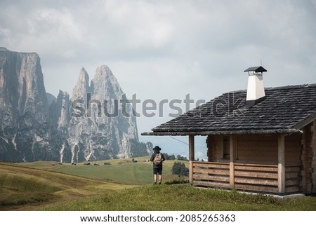 Hiker meditating wearing a hat under alp house enjoying high mountains landscape views in Alpe di Siusi - Seiser alm Dolomites - Aventure Vacation travel healthylife - Italy