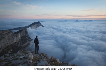 A hiker in the mountains looking over the clouds at dawn. Vercors, France.