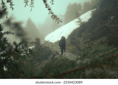 Hiker navigating a misty trail surrounded by snow and dense forest in a mountainous region - Powered by Shutterstock