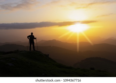 Hiker on the top of a mountain facing the sun.