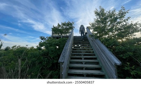 Hiker and photographer climbing a hawk watch platform in sunset. He is looking for birds on the nature trail. - Powered by Shutterstock