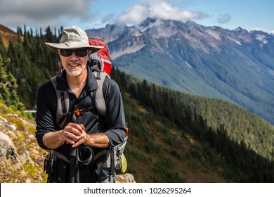 Hiker poses in front of mountain peaks range hiking backpacker old older aarp strong strength vital energetic landscape photography portrait background colorful adventure retired retirement outdoor 