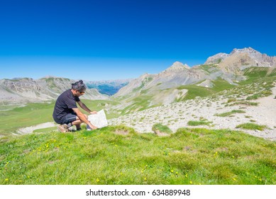 Hiker reading trekking map while resting at panoramic mountain spot. Outdoors activities, summer adventures and exploration on the Italian French Alps. Expansive view from the top.